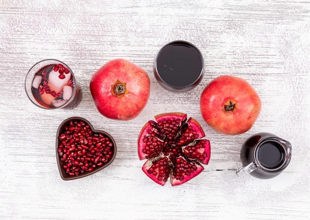 Free photo top view pomegranate juice and pomegranate seeds in heart shaped plate on white wooden table