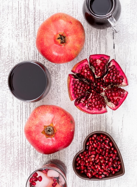 Free photo top view pomegranate juice and pomegranate seeds in heart shaped plate on white wooden table