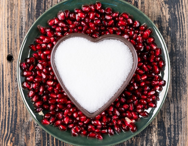 top view pomegranate in plate with heart shaped plate with sugar on wooden table