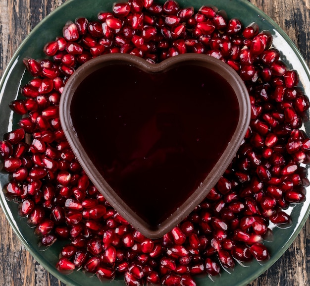 Top view pomegranate in plate with heart shaped plate on wooden surface