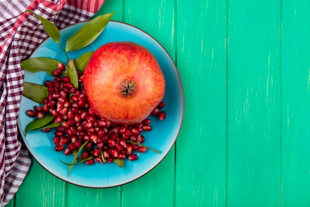 Top view of pomegranate and pomegranate berries in plate on plaid cloth and green surface