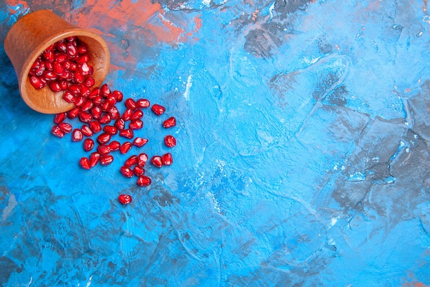 Free Photo top view pomegranate seeds in little wooden bowl on blue background with free place