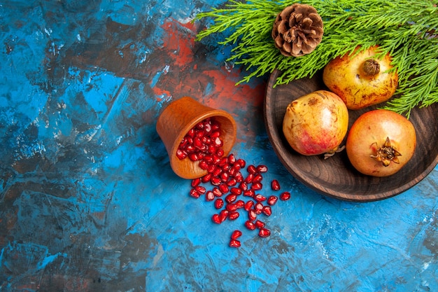 Free Photo top view pomegranate seeds placed in wooden cup with scattered seeds pomegranates on wooden plate pine tree branch on blue background