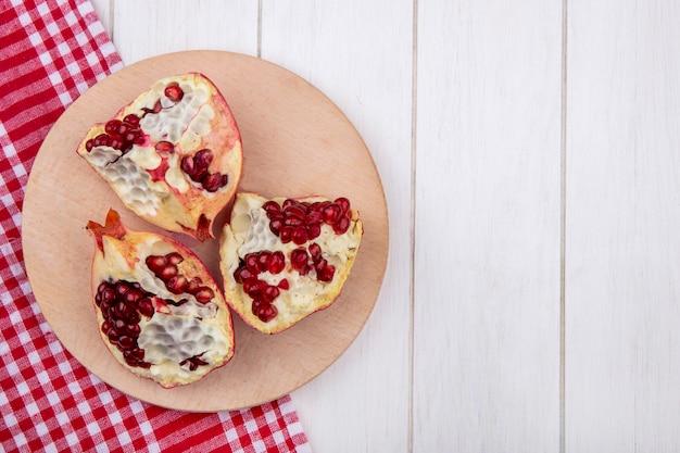 Free photo top view of pomegranate slices on a stand with a red checkered towel on a white surface