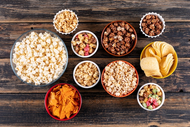 Top view of popcorn and chips in bowls on dark wooden  horizontal