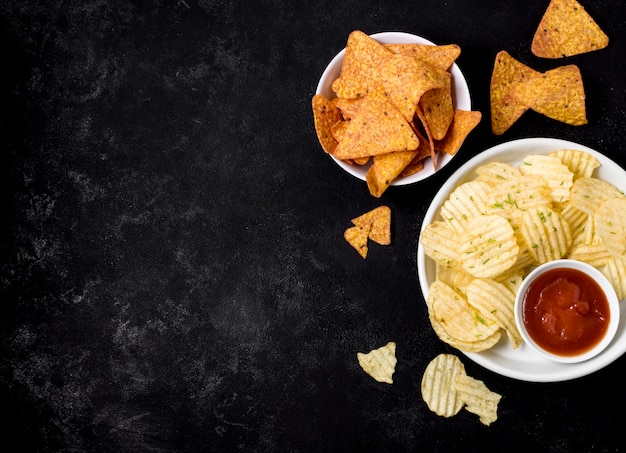 Top view of potato chips and nacho chips with ketchup