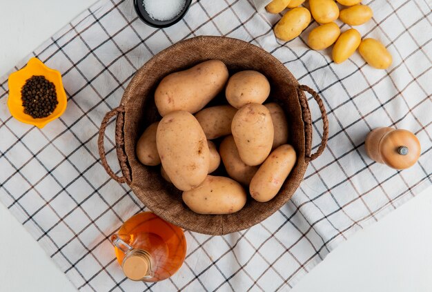 Top view of potatoes in basket with butter salt black pepper on plaid cloth and white surface