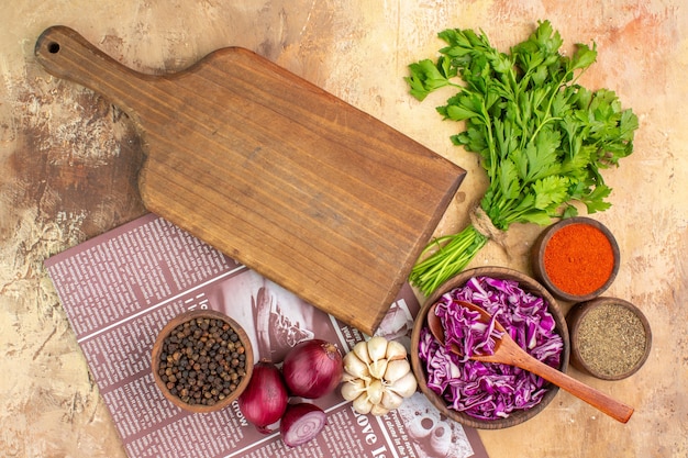 Top view prepare red onions garlic a bunch of parsley together with a bowl of black pepper turmeric ground pepper red cabbage for salad on a wooden table