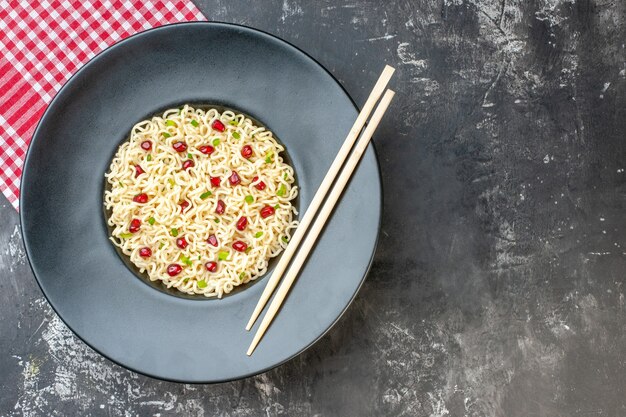 Top view ramen noodles on dark round plate red white checkered napkin chopsticks on dark background