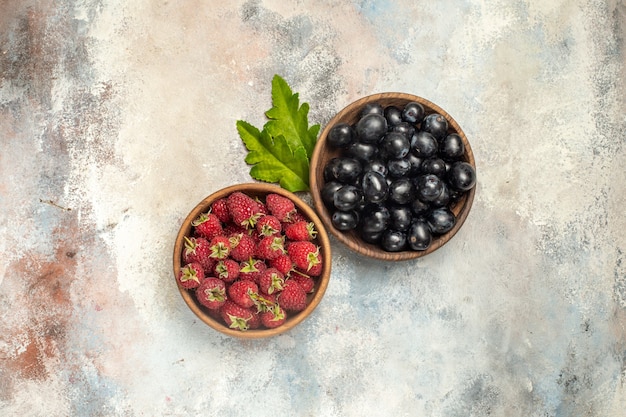 Free photo top view raspberries and grapes in bowls on grey isolated surface with free space