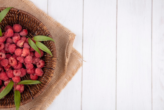 Free Photo top view of raspberries and leaves in basket on sackcloth and wooden surface