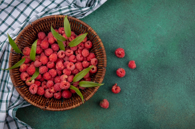 Free Photo top view of raspberries with leaves in basket on plaid cloth and green surface