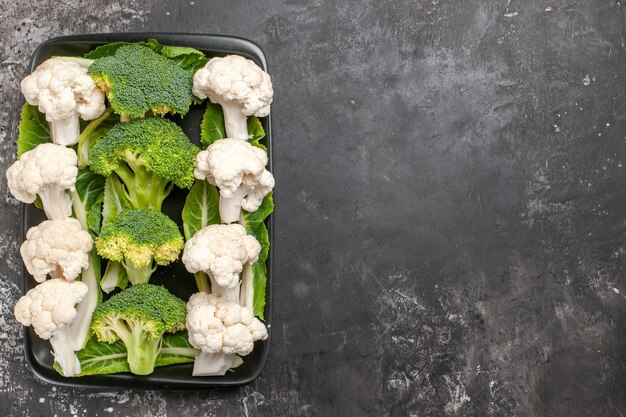 Top view raw broccoli and cauliflower on black rectangular plate on dark surface free space