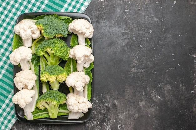 Free photo top view raw broccoli and cauliflower on black rectangular plate on green and white checkered napkin on dark surface with copy space