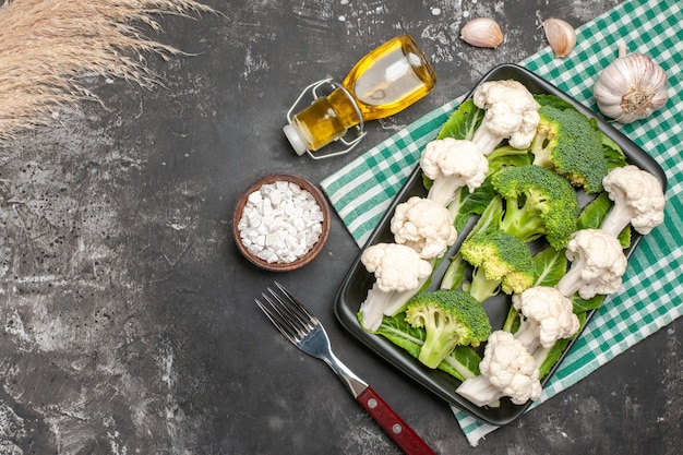 Free Photo top view raw broccoli and cauliflower on black rectangular plate on green and white checkered napkin fork oil garlic sea salt on dark surface free space