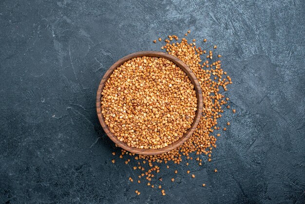 Top view raw buckwheat inside brown plate on grey space