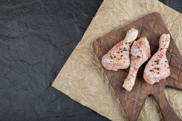 Top view raw chicken drumstick on wooden board.