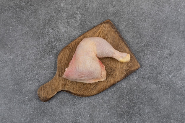 Top view of raw chicken leg on wooden cutting board