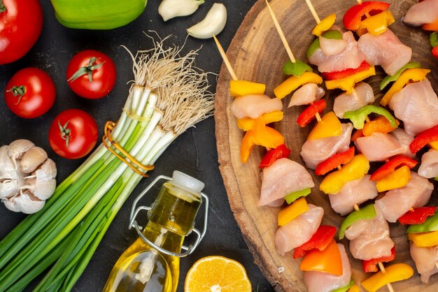 Top view raw chicken skewers on natural wood board vegetables on dark table