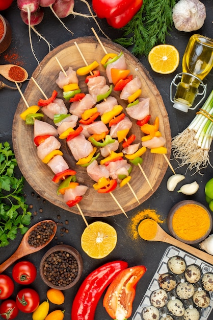 Free photo top view raw chicken skewers on natural wood board vegetables oil bottle quail eggs on dark table