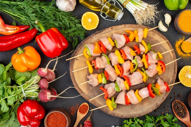 Free photo top view of raw chicken skewers on natural wood board vegetables oil bottle spices on dark table