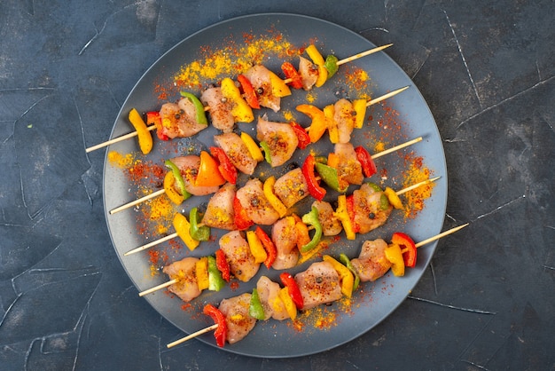 Top view raw chicken skewers with spices on wooden board on dark table