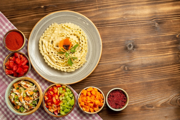 Top view raw dough pasta with vegetables and seasonings on a brown table dough raw food pasta meal