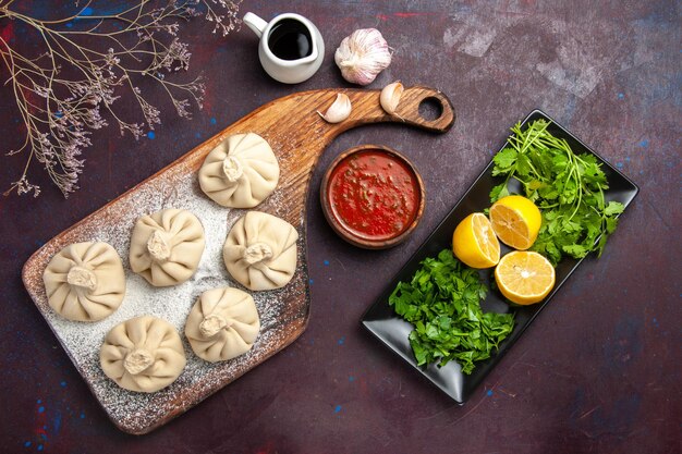 Top view of raw dumplings dough with tomato sauce and lemon slices on black