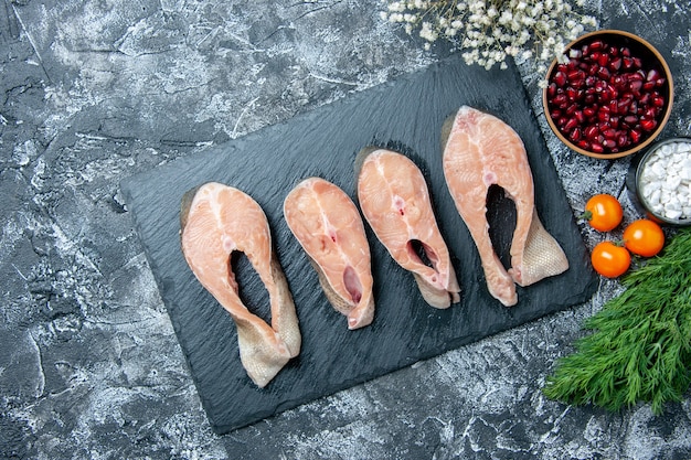 Free photo top view raw fish slices on black board vegetables small white flowers on table