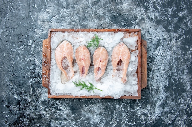 Free Photo top view raw fish slices with ice on wood serving board on grey background