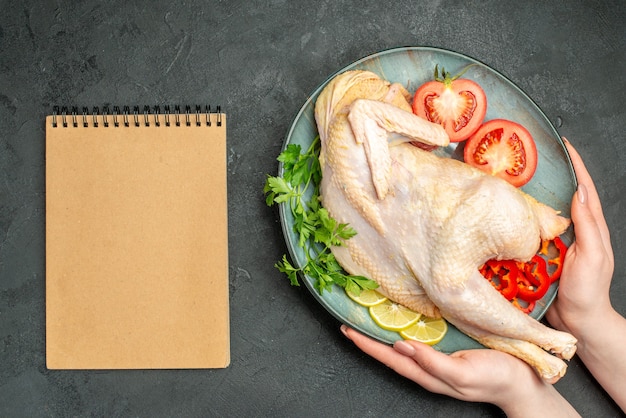 Top view raw fresh chicken inside plate with greens and vegetables on dark background