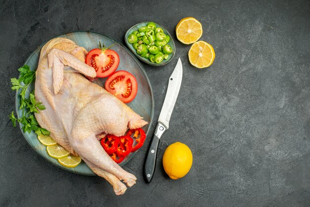 Top view raw fresh chicken inside plate with greens and vegetables on dark background