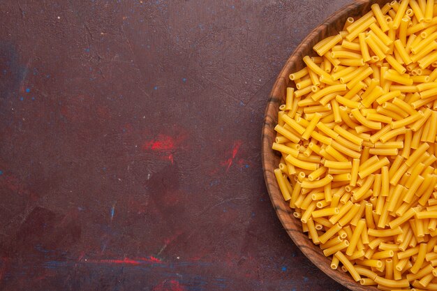 Top view raw italian pasta little formed on dark desk vegetables pasta meal food color