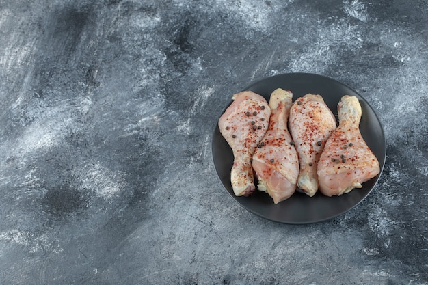 Free photo top view of raw marinated chicken legs on black plate over grey background.