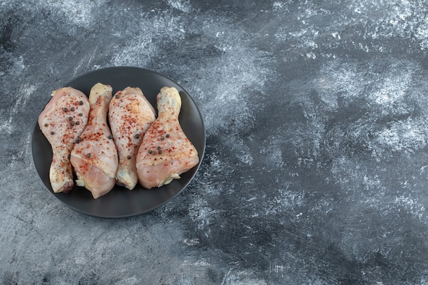 Top view of raw marinated chicken legs on black plate.