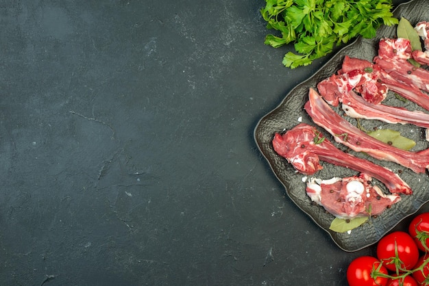 Top view raw meat slices with greens and red tomatoes on dark background dish meat butcher meal salad food cooking