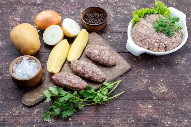 Free photo top view raw meat with raw potatoes salt onion and greens on the brown rustic wooden desk meat potato dish meal dinner