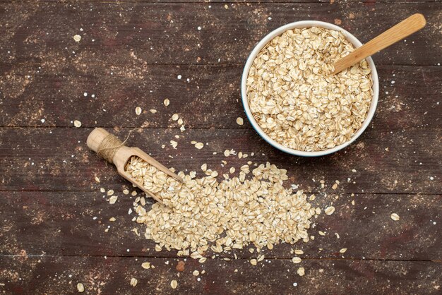 Top view raw oatmeal inside white plate on brown, food raw health breakfast