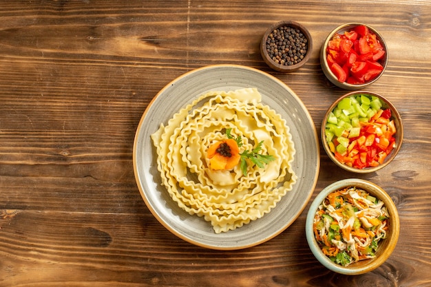 Top view raw pasta dough with seasonings and vegetables on brown background dough meal food raw pasta