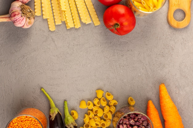 A top view raw pasta yellow dry long italian pasta along with red tomatoes eggplants carrots and garlic isolated on the grey background vegetables food meal