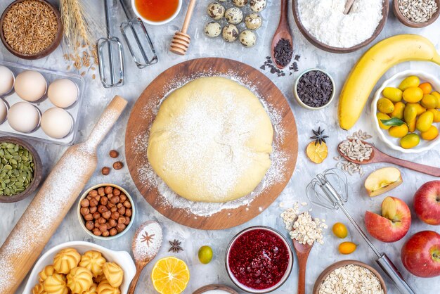 Top view of raw pastry on round wooden board grater and set of foods on ice background