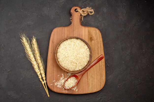 Top view of raw rice inside wooden brown plate on dark grey surface