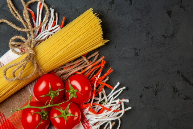 Top view of raw spaghetti and tied with string and fresh tomatoes on black