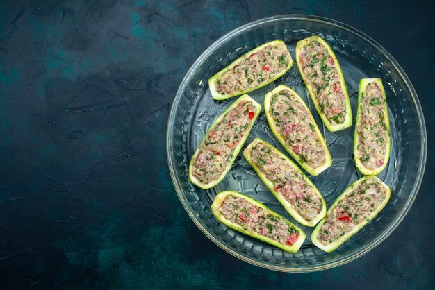 Top view of raw squashes with spicy minced meat inside glass plate on dark blue surface