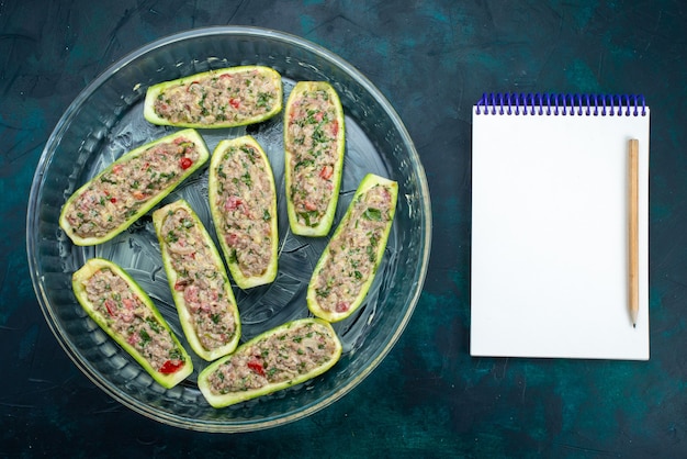 Free photo top view of raw squashes with spicy minced meat inside glass plate on the dark blue surface