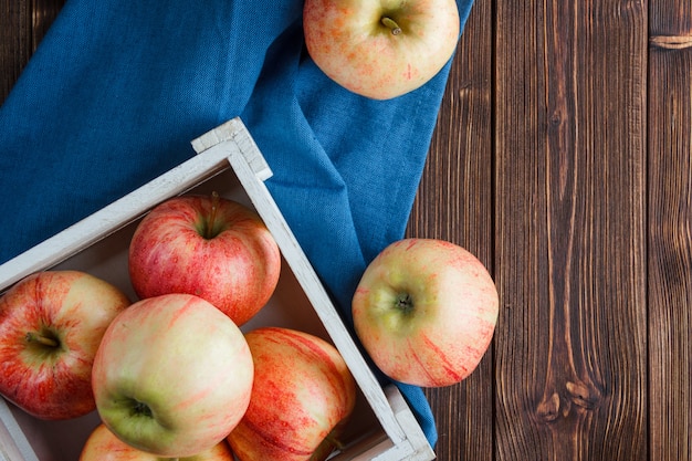 Top view red apples in wooden box and around on blue cloth and wooden background. horizontal