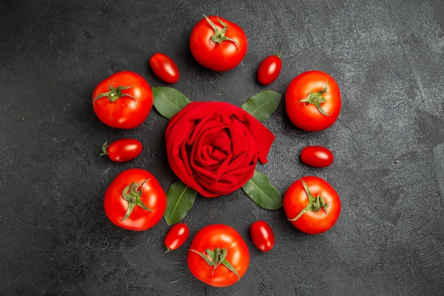 Top view red and cherry tomatoes around a towel in rose shape and bay leaves on dark ground with copy space