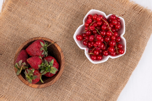 Top view red currant in a bowl with strawberries on a beige napkin