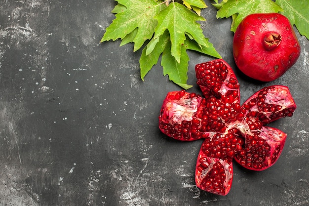 Top view red fresh pomegranate with green leaves on a dark surface