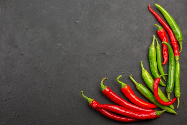 Top view red and green peppers at the bottom right of black table with free space